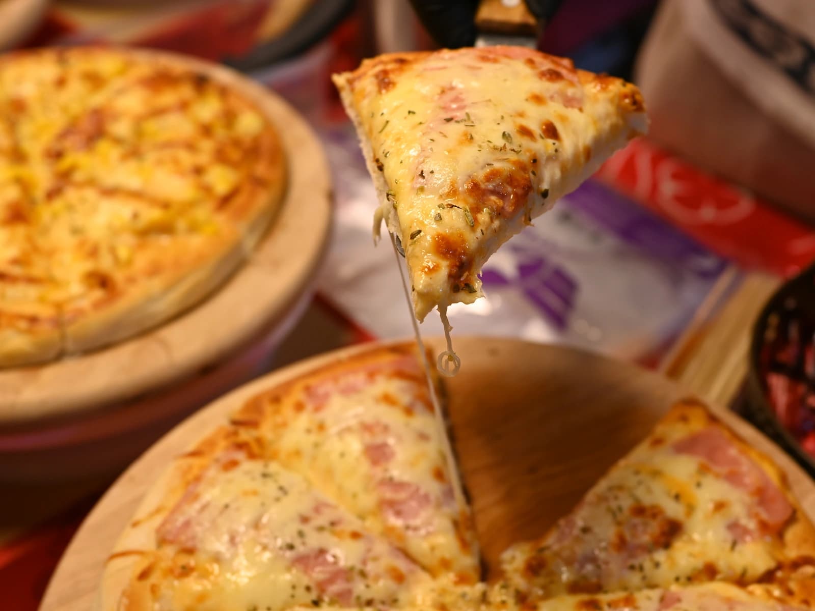 Close-up of a cheesy wood-fired pizza slice being lifted, with melted cheese stretching from the pie below